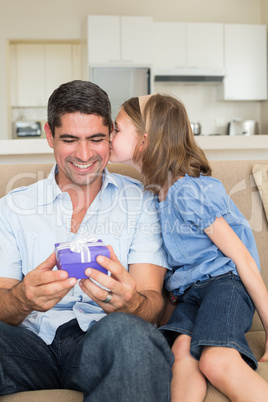 Girl kissing father holding gift box on sofa