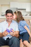Girl kissing father holding gift box on sofa