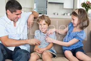 Father and daughter tickling boy on sofa