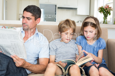Father with newspaper while children reading book