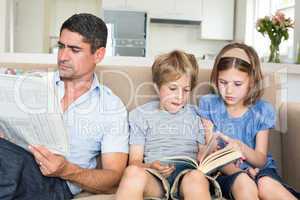 Father with newspaper while children reading book