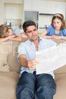 Bored children looking at father reading newspaper