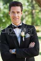 Confident groom with arms crossed in garden