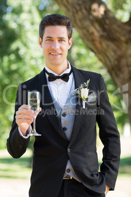 Sophisticated groom holding champagne flute in garden
