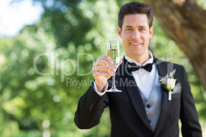 Smiling groom holding champagne flute in garden