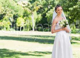 Attractive bride holding flowers in park