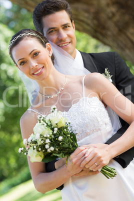 Loving groom embracing bride from behind in garden