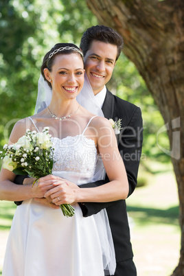 Happy groom embracing bride from behind in garden