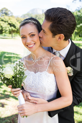 Groom kissing bride on cheek in garden