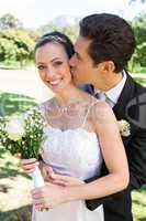 Groom kissing bride on cheek in garden