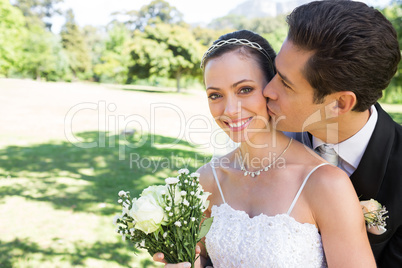 Groom kissing beautiful bride on cheek in garden