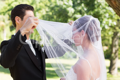 Loving groom unveiling bride in garden