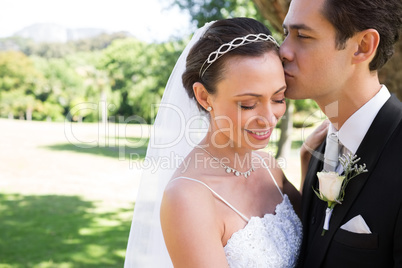 Groom kissing shy bride on head in garden