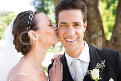 Bride kissing groom on cheek in garden
