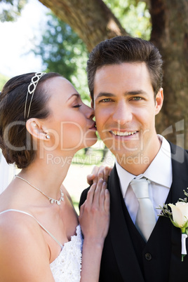Beautiful bride kissing groom on cheek in garden