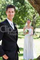Happy groom with bride standing in background at garden