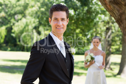 Confident groom with bride in background at garden
