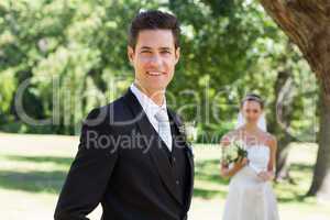 Confident groom with bride in background at garden