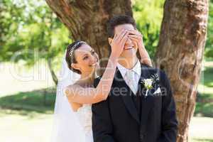 Bride covering eyes of groom in garden