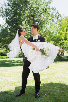 Happy groom carrying bride in arms at garden