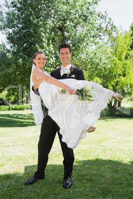 Happy groom lifting bride in arms at garden