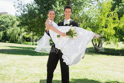 Young groom lifting bride in arms at garden