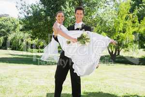 Young groom lifting bride in arms at garden