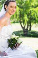 Bride holding bouquet while sitting in garden