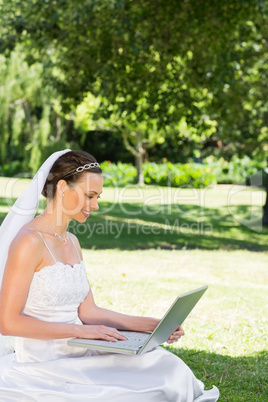 Bride using laptop on grass at garden