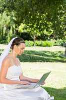 Bride using laptop on grass at garden