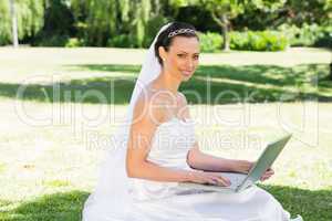 Smiling bride using laptop in garden