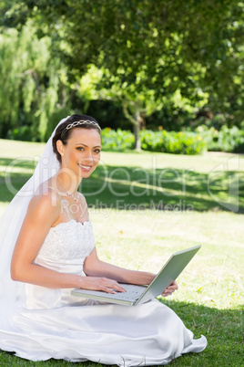 Beautiful bride with laptop sitting on grass