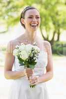 Bride holding bouquet while laughing in garden