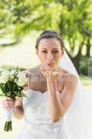 Bride with bouquet blowing kiss in garden