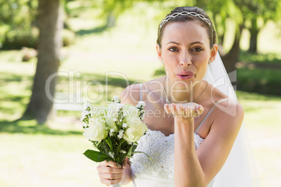Beautiful bride with bouquet blowing kiss in garden