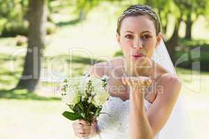 Beautiful bride with bouquet blowing kiss in garden