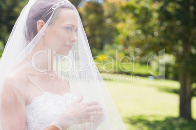 Young bride looking away through veil in garden