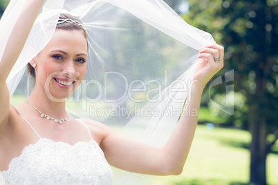 Happy young bride unveiling self in garden