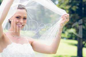 Happy young bride unveiling self in garden
