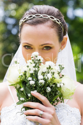 Young bride peeking over bouquet in garden