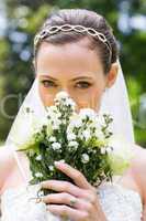 Young bride peeking over bouquet in garden