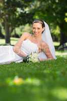 Happy bride lying on grass in park