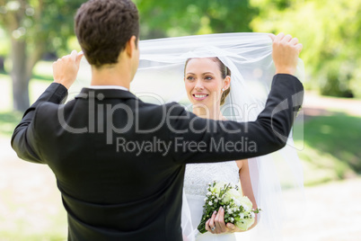 Loving groom lifting veil of bride