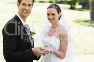 Groom placing ring on brides finger at park