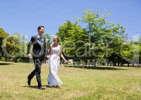 Bride and groom holding hands walking in park