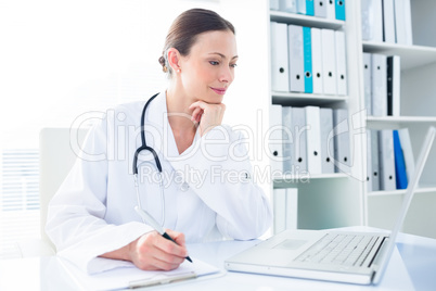 Doctor writing while using laptop