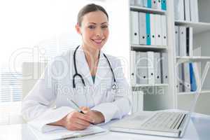 Doctor with laptop and clipboard sitting at desk