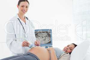 Smiling doctor performing ultrasound on pregnant woman