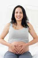 Happy pregnant woman making heart shape on belly