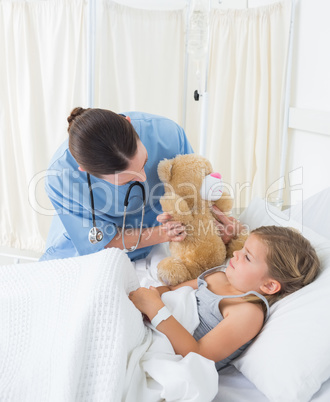 Doctor with teddy bear entertaining sick girl